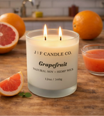 J | F Candle Co. Grapefruit soy candle with a lit wick in a frosted glass jar, styled on a light kitchen countertop with fresh grapefruit, citrus accents, and soft natural light in a clean, upscale setting
