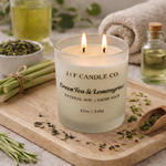Luxury green tea and lemongrass soy candle by J | F Candle Co with double lit wicks in frosted glass jar, styled with lemongrass and loose tea leaves on a wooden tray in a spa-inspired setting