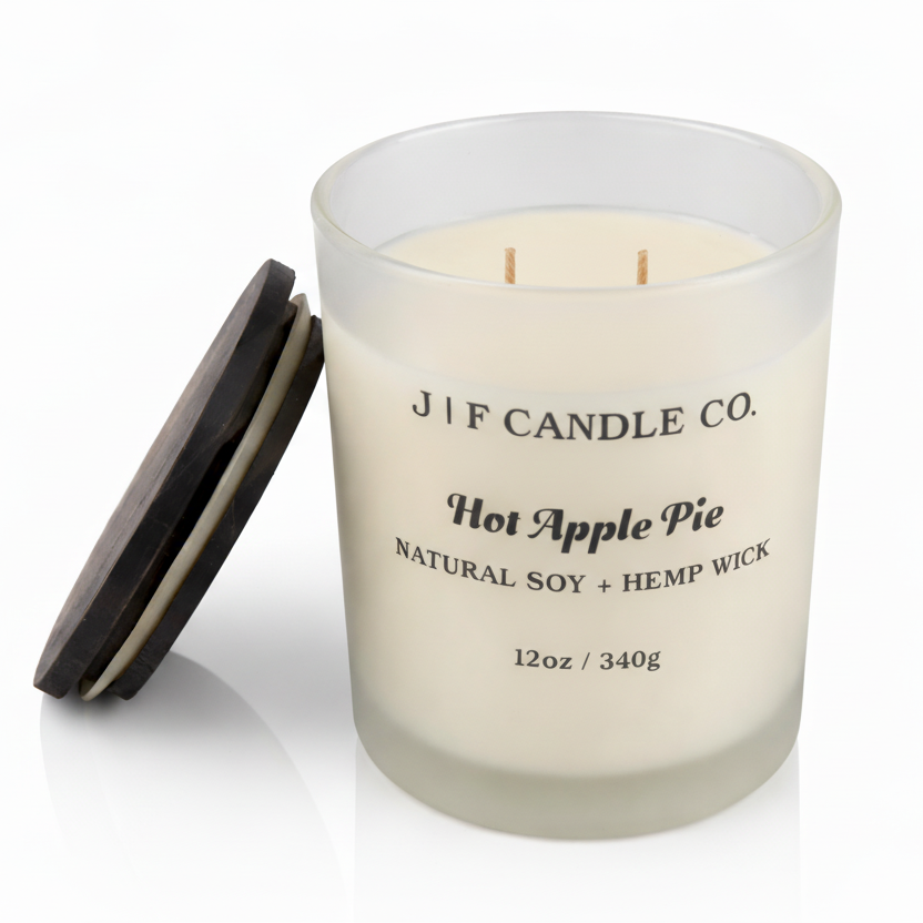 J | F Candle Co. Hot Apple Pie 12 oz soy candle in a frosted glass jar with the dark wood lid placed beside it on a clean white background with a soft reflection.