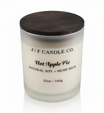 J | F Candle Co. Hot Apple Pie 12 oz soy candle in a frosted glass jar with dark wood lid on a clean white background with a soft reflection.