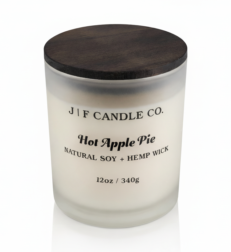 J | F Candle Co. Hot Apple Pie 12 oz soy candle in a frosted glass jar with dark wood lid on a clean white background with a soft reflection.