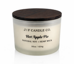 J | F Candle Co. Hot Apple Pie 16 oz soy candle in a frosted glass jar with dark wood lid on a clean white background with a soft reflection.