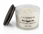 J | F Candle Co. Hot Apple Pie 16 oz three-wick soy candle in a frosted glass jar with the dark wood lid placed beside it on a clean white background with a soft reflection.