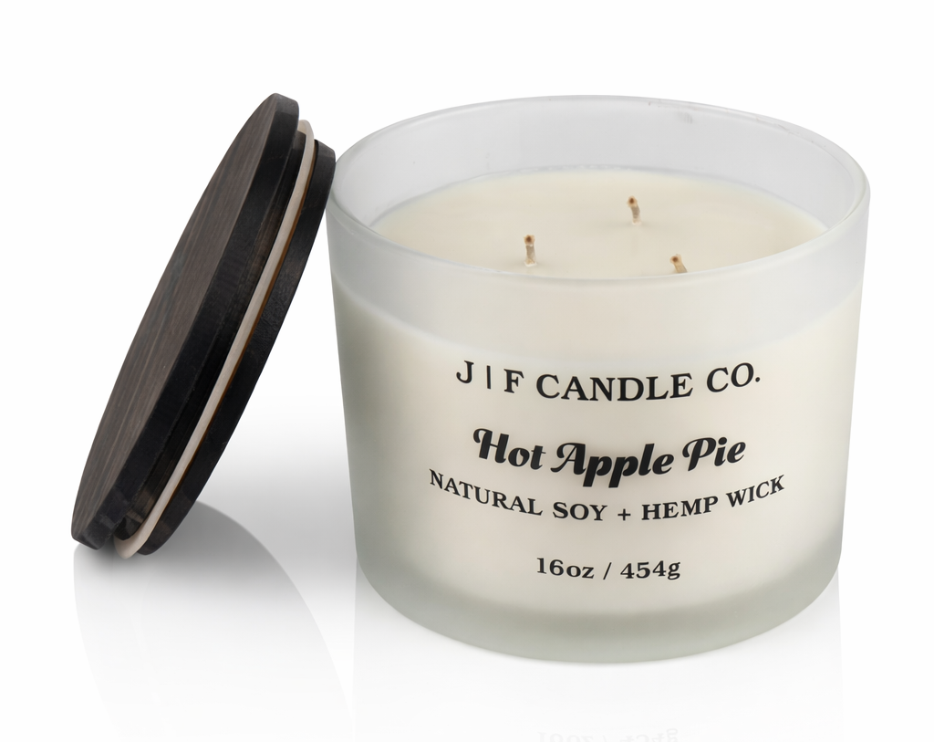J | F Candle Co. Hot Apple Pie 16 oz three-wick soy candle in a frosted glass jar with the dark wood lid placed beside it on a clean white background with a soft reflection.