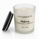 J | F Candle Co Mulberry luxury soy candle in 12oz frosted glass jar with wooden lid beside candle and soft reflection on clean white background