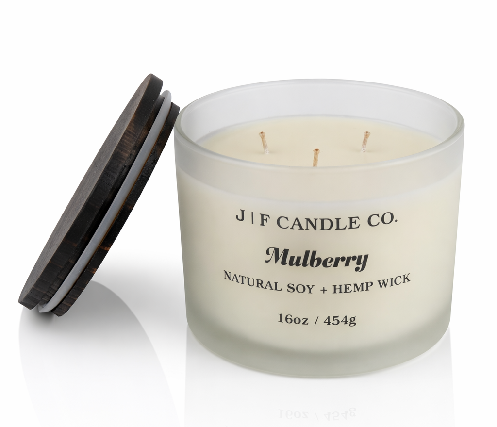 J | F Candle Co Mulberry luxury soy candle in 16oz frosted glass jar with three wicks and wooden lid beside candle on clean white background with soft reflection