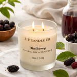 J | F Candle Co. Mulberry luxury soy candle in a frosted glass jar, lit and styled on a white marble tray with fresh mulberries and green leaves.