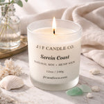 Serein Coast luxury soy candle by J | F Candle Co. lit on a marble surface with soft coastal props and light sea glass accents.