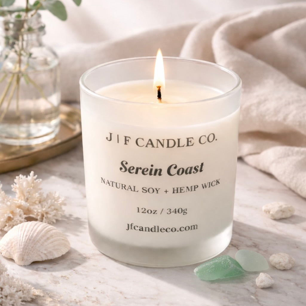 Serein Coast luxury soy candle by J | F Candle Co. lit on a marble surface with soft coastal props and light sea glass accents.