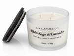 White Sage & Lavender 16 oz three-wick soy candle by J | F Candle Co. in frosted glass jar with wooden lid beside it, clean white background with soft reflection, hand-poured luxury candle